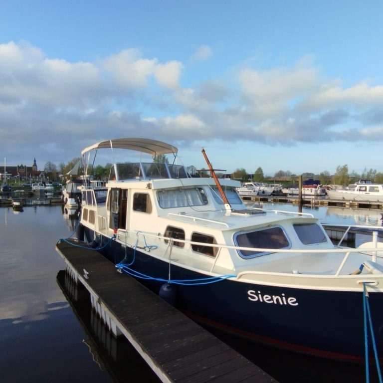 Ein Boot namens "Sienie" liegt an einem Yachthafen bei wolkigem Himmel.