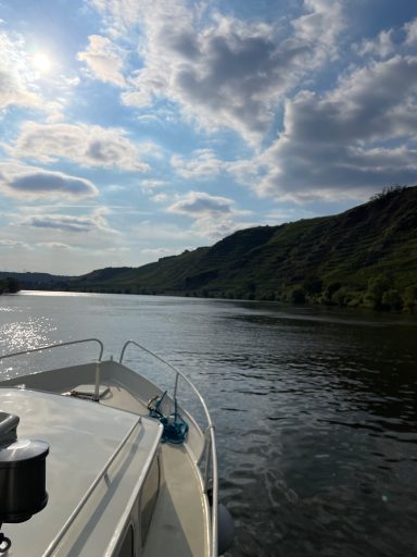 Ein Boot auf einem ruhigen Fluss, umgeben von sanften Hügeln und bewölktem Himmel.