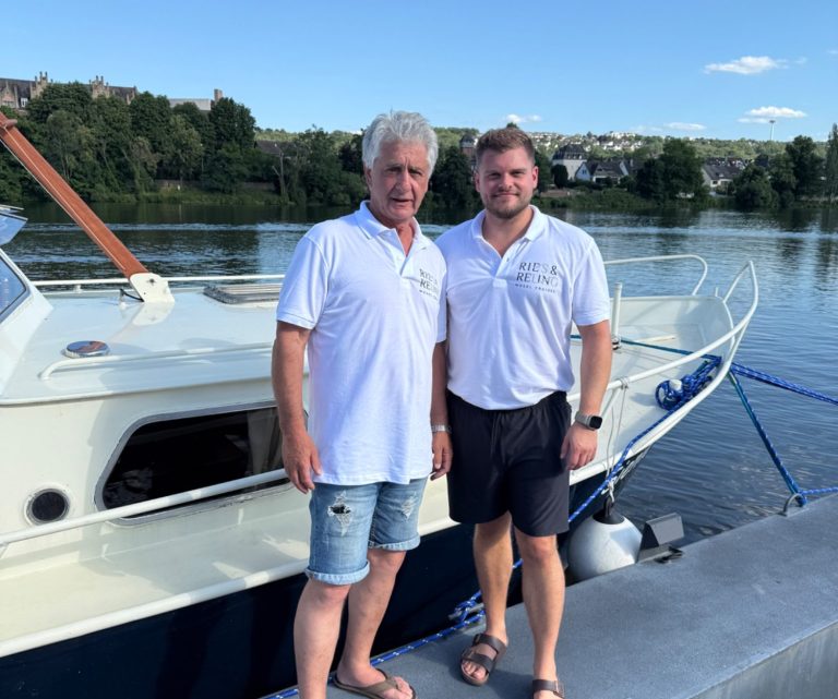 Gruppe von Menschen feiert mit Getränken auf einem Boot an einem sonnigen Tag.