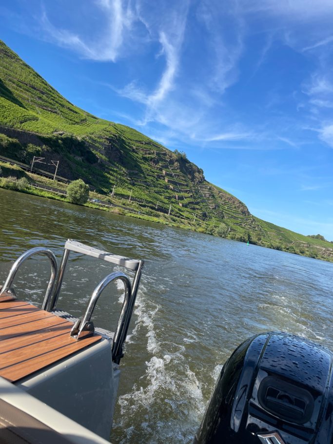 Boot auf einem Fluss mit grünen Hügeln im Hintergrund und blauem Himmel.