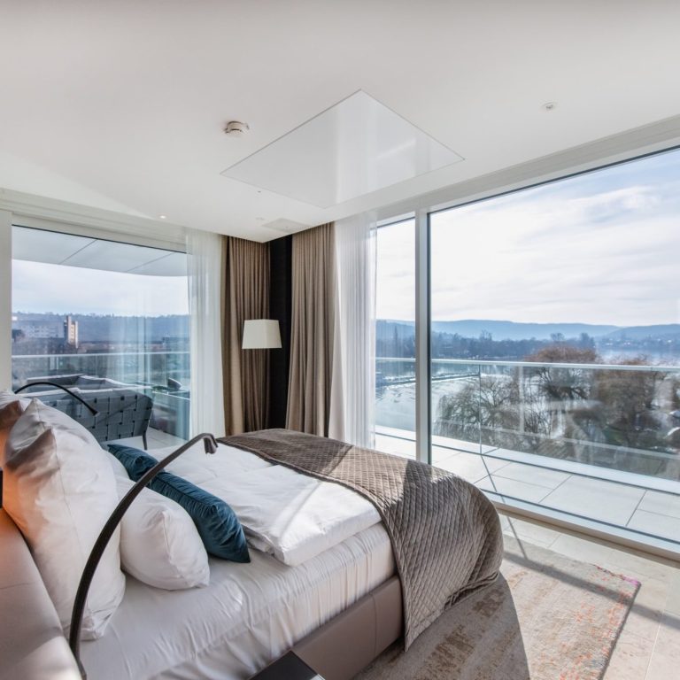 Helles, modernes Schlafzimmer mit Aussicht auf ein Gewässer und große Fenster.