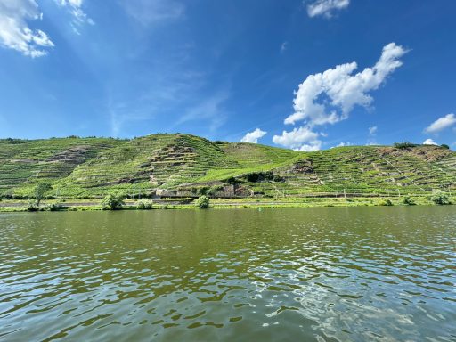 Grüne Hügel spiegeln sich im ruhigen Wasser eines Flusses unter klarem Himmel.