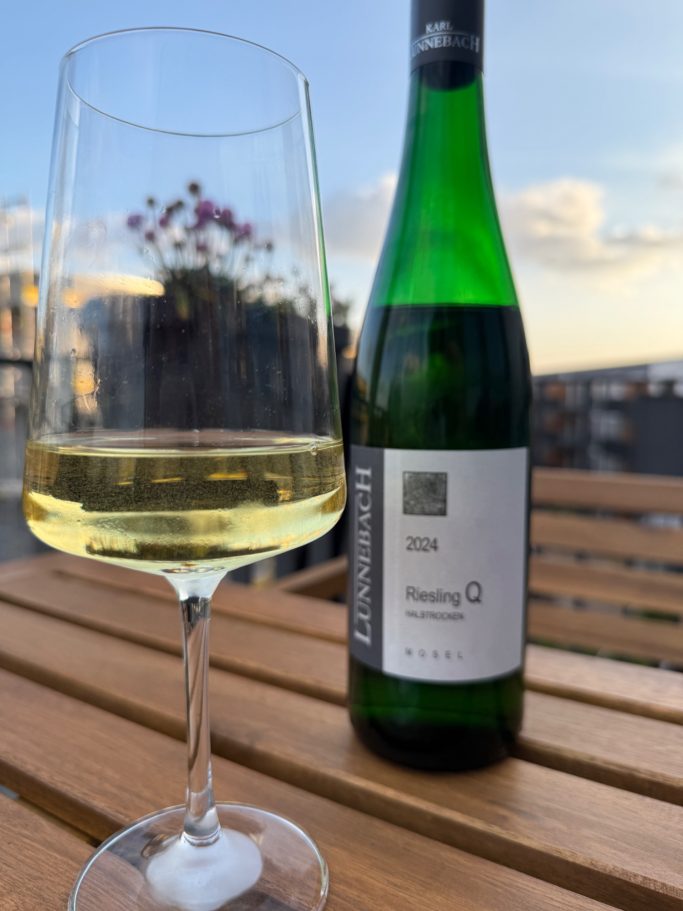 Weißwein im Glas mit einer Flasche im Hintergrund auf einem Holztisch.